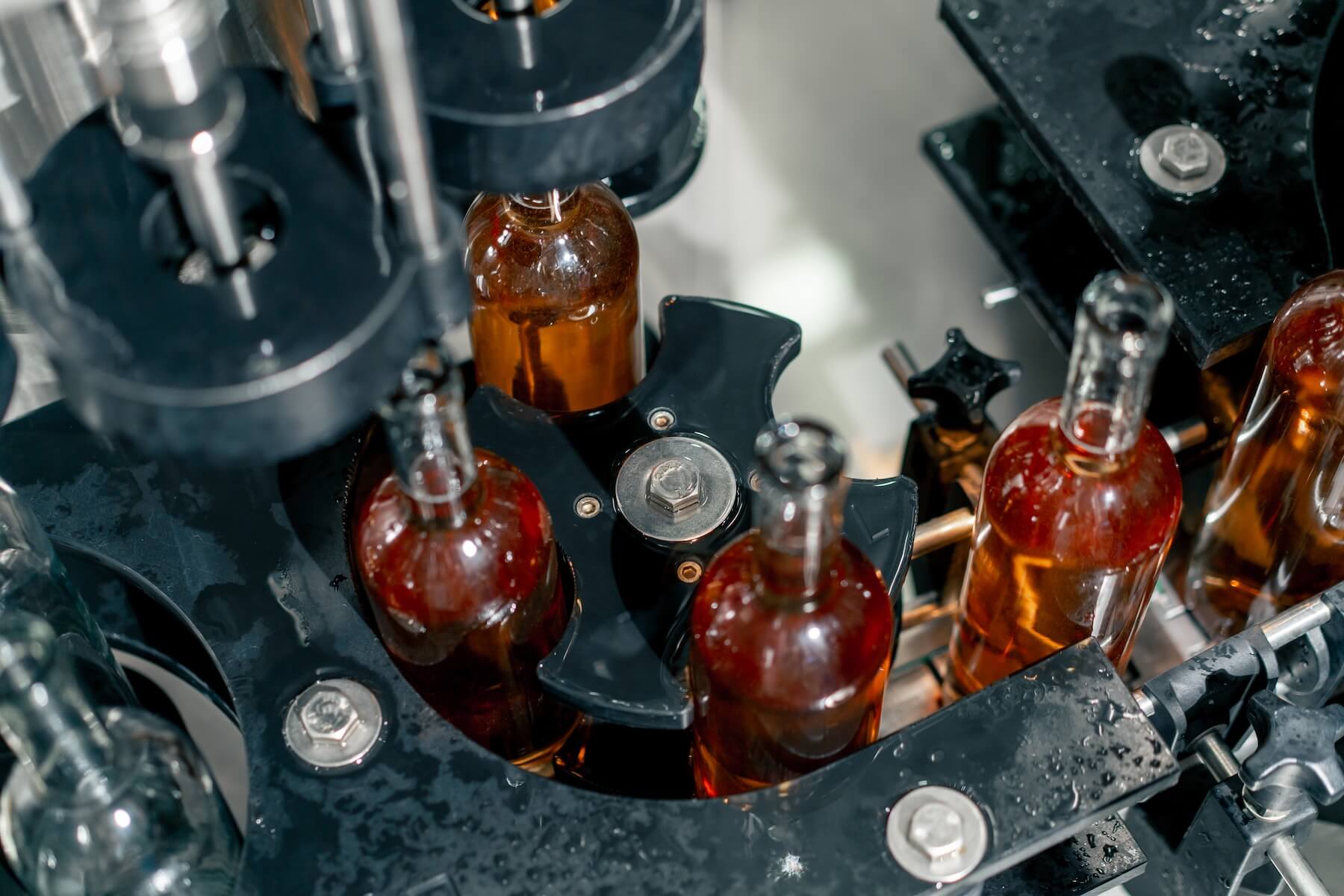 Transparent glass bottles filled with wine are arranged in a row on the packaging line to be closed with wooden stoppers